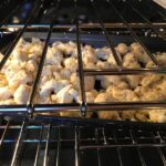 Coconut Cauliflower Bites baking in the oven. They have a slightly sweet and salty crunch outside from the shredded coconut and panko mixture.  The inside is soft and creamy.  Dip in the Sriracha Mayo.  Baked, not fried, so healthy!  Easy to make, easy to eat! #cauliflowerrecipes #healthyrecipes #sidedishes #appetizers #healthysnacks