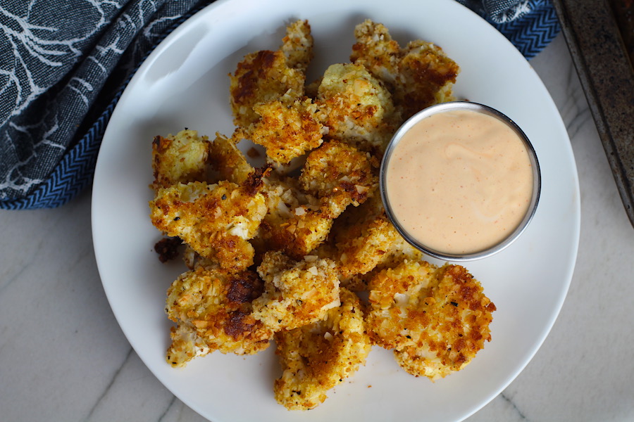 Baked Coconut Cauliflower Bites on plate with Sriracha Mayo dipping sauce.  They have a slightly sweet and salty crunch outside from the shredded coconut and panko mixture.  The inside is soft and creamy.  Dip in the Sriracha Mayo. 