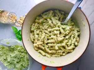 Broccoli Pesto Pasta in pot with spoon with pine nuts and basil on counter. It's delicious AND good for you!  It has all of the classic pesto flavors from garlic, basil, parmesan cheese, and pine nuts.  But the flavor is a bit more mellow by adding broccoli! #broccolirecipes #pesto #pasta #easydinner #dinnerideas #familydinner