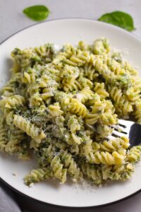 Broccoli Pesto Pasta on a plate with fork in pasta. It's delicious AND good for you!  It has all of the classic pesto flavors from garlic, basil, parmesan cheese, and pine nuts.  But the flavor is a bit more mellow by adding broccoli! #broccolirecipes #pesto #pasta #easydinner #dinnerideas #familydinner