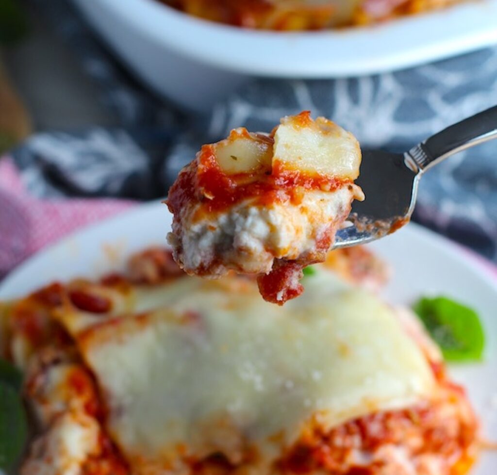 Chicken Lasagna on a plate with fork holding bite up. from the dish. This Easy ITalian Sausage Lasagne Recipe is the stuff that dreams are made of.  Layers of pasta, creamy ricotta, salty chewy mozzarella, salty and hearty Italian Sausage, and sweet and tangy tomato sauce.