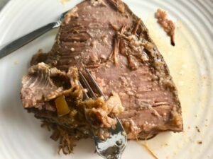 Fork scraping off fat layer from cooked brisket for Smoky Pulled Beef Brisket.  It's smokey, savory, tender, moist, and full of flavor. In a delicious sauce, it goes great on a sandwich, over polenta, on rice, or potatoes. #slowcooker #crockpot #brisket #beefbrisket #pulledbeef #pulledpork