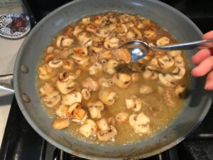Spoon adding garlic to mushrooms in skillet for Chicken Stroganoff with mushrooms, and spinach.  It has a thick, creamy, savory mushroom sauce with a touch of tangy sour cream. #chickendinners #chickenrecipes #familydinners #dinnerideas