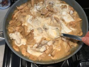 Mixing sour cream into chicken and mushroom sauce in skillet for Chicken Stroganoff with mushrooms, and spinach.  It has a thick, creamy, savory mushroom sauce with a touch of tangy sour cream. #chickendinners #chickenrecipes #familydinners #dinnerideas