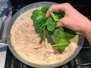 Adding spinach to chicken and mushroom sauce in skillet for Chicken Stroganoff with mushrooms, and spinach.  It has a thick, creamy, savory mushroom sauce with a touch of tangy sour cream. #chickendinners #chickenrecipes #familydinners #dinnerideas