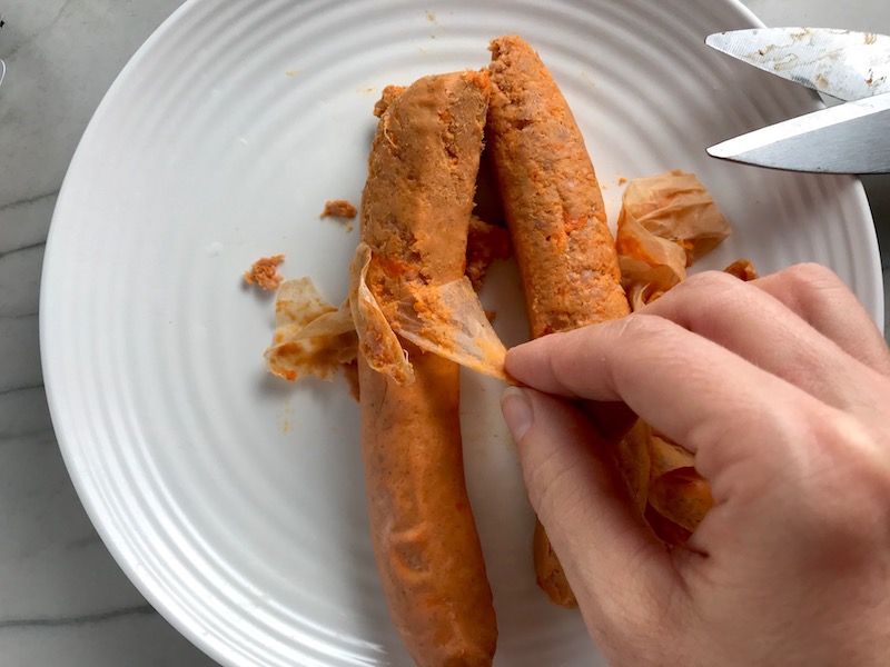 Hand removing the casing from chorizo for Patatas Bravas with chorizo and creamy Paprika aioli. This Patatas Bravas Recipe, or Spicy Potatoes, is easy, indulgent, and utterly delicious!  #potatorecipes #potatoes #potatosidedishes #patatasbravas #skilletpotatoes #sidedishes #chorizo