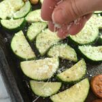 Hand sprinkling parmesan on zucchini for Mediterranean SHEET PAN DINNER with chicken sausage, parmesan zucchini. and crispy chickpeas. Serve over quinoa with dollops of seasoned Ricotta. #sheetpandinner #chickpeas