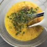 Pouring milk into eggs with scallions in bowl for Slow Cooker Egg Casserole with Chorizo, Potatoes and both cheddar and manchego cheeses. IT COOKS WHILE YOU SLEEP! #eggs #eggcasseroles #eggrecipes #breakfastideas #holidayrecipe
