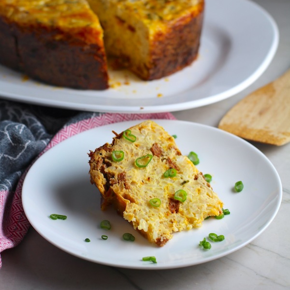 Piece of Slow Cooker Eggs Casserole on a plate with scallions. It has Chorizo, Potatoes and both cheddar and manchego cheeses. IT COOKS WHILE YOU SLEEP! #eggs #eggcasseroles #eggrecipes #breakfastideas