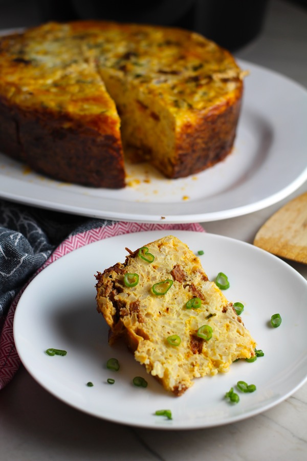 Piece of Slow Cooker Egg Casserole on a plate with scallions. It has Chorizo, Potatoes and both cheddar and manchego cheeses. IT COOKS WHILE YOU SLEEP! #eggs #eggcasseroles #eggrecipes #breakfastideas #holidayrecipes