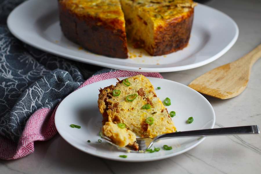 Piece of Slow Cooker Egg Casserole on a plate with scallions. It has Chorizo, Potatoes and both cheddar and manchego cheeses. IT COOKS WHILE YOU SLEEP! #eggs #eggcasseroles #eggrecipes #breakfastideas #holidayrecipes