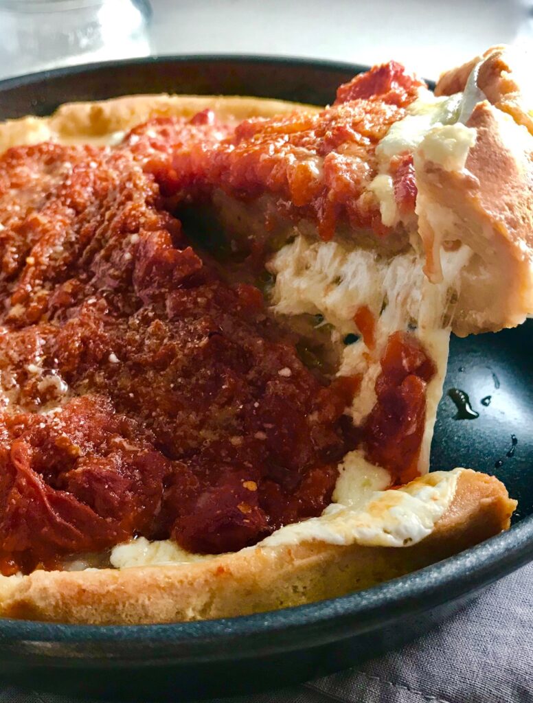 Spatula lifting slice Chicago Style pizza with tomatoes on top.This Chicago Style Pizza is a lighter and healthier version, but still AMAZING! It still has all of the gooey mozzarella cheese, but uses homemade turkey Italian Sausage, that's so delicious!