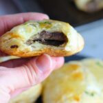 Hand holding Mini Beef Wellington Bite with bite taken. Buttery Puff Pastry is filled with a creamy mushroom and parmesan filling and tender beef filet.  #appetizers #partyfood #beefrecipes #appetizerrecipes
