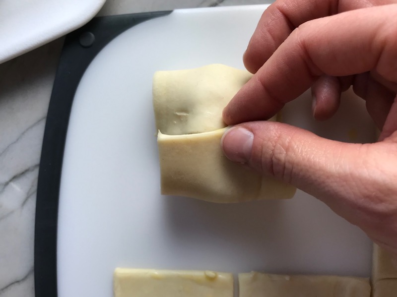 Hand folding puff pastry over filling for Mini Beef Wellington Bites. They are flaky and buttery Puff Pastry is filled with a creamy mushroom and parmesan filling and tender beef filet.  #appetizers #partyfood