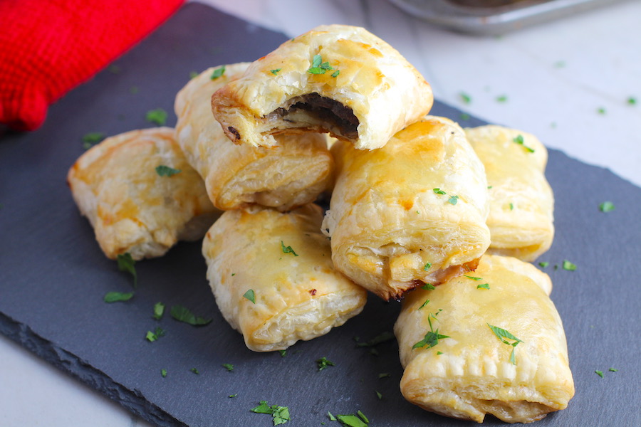 Mini Beef Wellington Bites stacked on platter. They are flaky and buttery on the outside. Puff Pastry is filled with a creamy mushroom and parmesan filling and tender beef filet.  #appetizers #partyfood