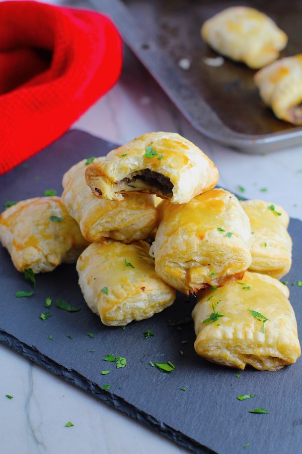 Mini Beef Wellington Bites stacked on platter. They are flaky and buttery on the outside. Puff Pastry is filled with a creamy mushroom and parmesan filling and tender beef filet.  #appetizers #partyfood