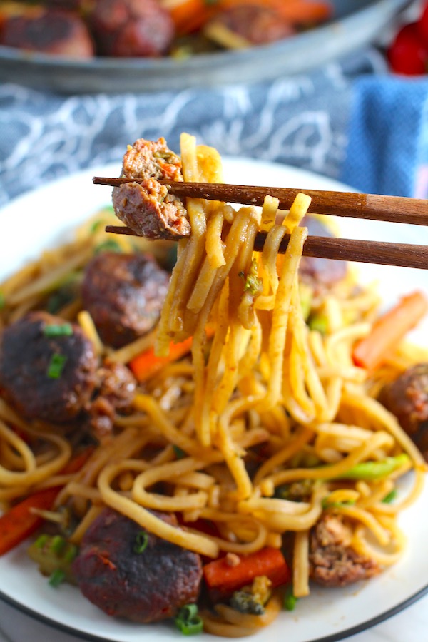 Chopsticks with bite of Teriyaki Meatballs with Veggie Stir Fry, and rice noodles on a plate.  #asianmeatballs #teriyaki #noodles #familydinner #easydinners #dinnerideas