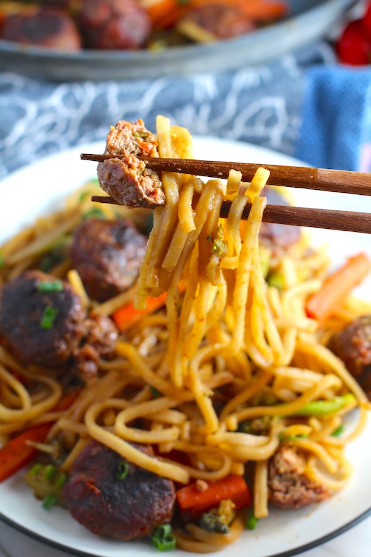 Chopsticks with bite of Teriyaki Meatball Stir Fry with Veggie Stir Fry, and rice noodles on a plate.  #asianmeatballs #teriyaki #noodles #familydinner #easydinners #dinnerideas