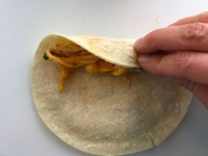 Rolling corn tortilla for Chicken Taquitos. Corn tortillas are filled with smoky taco seasoned shredded chicken, and creamy cheddar cheese.  #dinnerideas #familydinner #chickenrecipes #chickendinner #tacos #taquitos