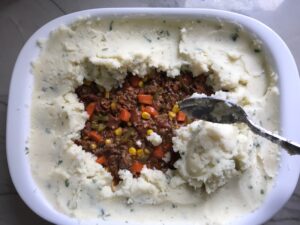 Covering filling with potatoes for Cottage Pie recipe.  It has Spanish Chorizo and ground beef cooked in a rich and savory gravy with veggies and herbs.  Creamy mashed potatoes sit on top with manchego, parmesan, and garlic. #dinnerideas #cottagepie #shepherdspie