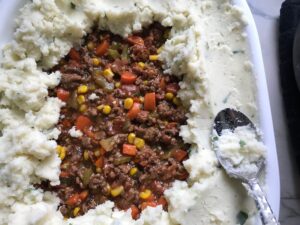 Covering filling with potatoes for Cottage Pie recipe.  It has Spanish Chorizo and ground beef cooked in a rich and savory gravy with veggies and herbs.  Creamy mashed potatoes sit on top with manchego, parmesan, and garlic. #dinnerideas #cottagepie #shepherdspie