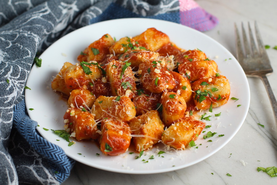 Cauliflower Gnocchi in tomato sauce on plate with parmesan and parsley. They are soft, silky, buttery, and melt-in-your-mouth! Made with cauliflower, they're a healthier version to traditional gnocchi! Add my simple Garlic Butter Sauce or Tomato Sauce and they are heaven.  #dinnerideas #gnocchi #cauliflower