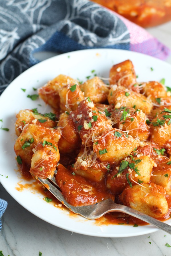 Cauliflower Gnocchi in tomato sauce on plate with parmesan and parsley. They are soft, silky, buttery, and melt-in-your-mouth! Made with cauliflower, they're a healthier version to traditional gnocchi! Add my simple Garlic Butter Sauce or Tomato Sauce and they are heaven.  #dinnerideas #gnocchi #cauliflower