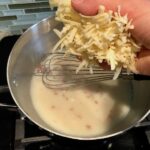 Adding shredded cheese to sauce for Bacon Mac and Cheese. It has a creamy and cheesy sauce with a touch of smokiness from the bacon, coats each piece of pasta.  On top, crispy crunchy, indulgent bacon fat cracker crumbs!