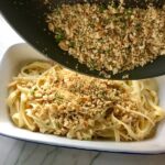 Pouring cracker crumbs over pasta for Bacon Mac and Cheese. It has a creamy and cheesy sauce with a touch of smokiness from the bacon, coats each piece of pasta.  On top, crispy crunchy, indulgent bacon fat cracker crumbs!