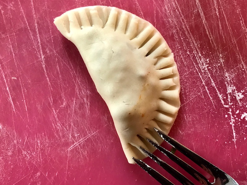 Fork pressing edges around Ground Beef Empanada. Flaky, buttery pastry on the outside with a savory, smokey, salty ground beef filling.