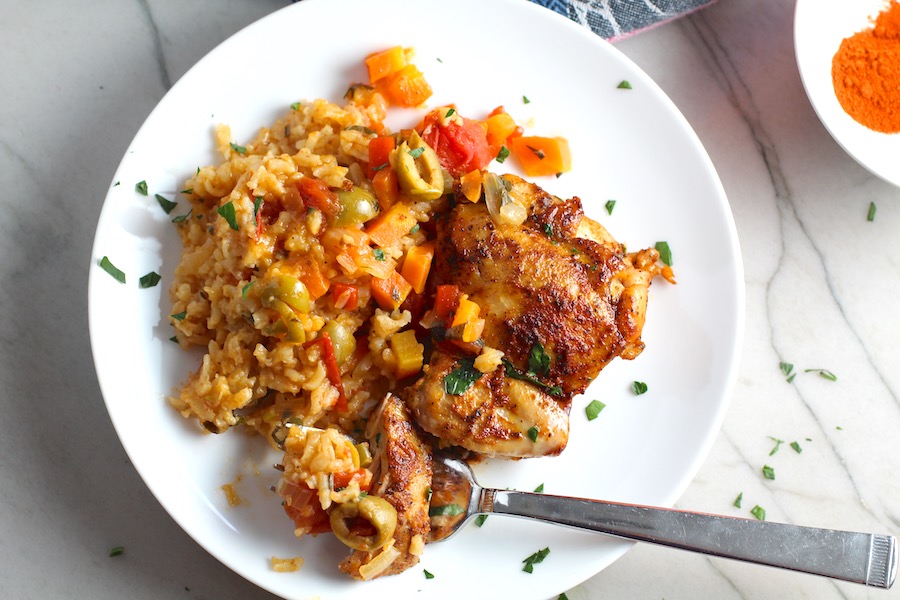 Spanish Chicken and Rice on plate with fork. It's hearty, smokey, and delicious! Paprika spice blend rubbed chicken thighs are seared then cooked with rice, onions, carrots, garlic, tomatoes, and olives for unbelievable flavor! #easydinners #chickenrecipes