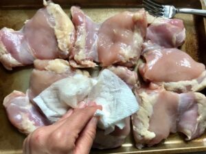 Patting skinless chicken thighs with paper towel for Spanish Chicken and Rice. It's hearty, smokey, and delicious! Paprika spice blend rubbed chicken thighs are seared then cooked with rice, onions, carrots, garlic, tomatoes, and olives for unbelievable flavor! #easydinners #chickenrecipes