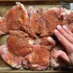 Rubbing seasoning on raw chicken thighs for Spanish Chicken and Rice. It's hearty, smokey, and delicious! Paprika spice blend rubbed chicken thighs are seared then cooked with rice, onions, carrots, garlic, tomatoes, and olives for unbelievable flavor! #easydinners #chickenrecipes