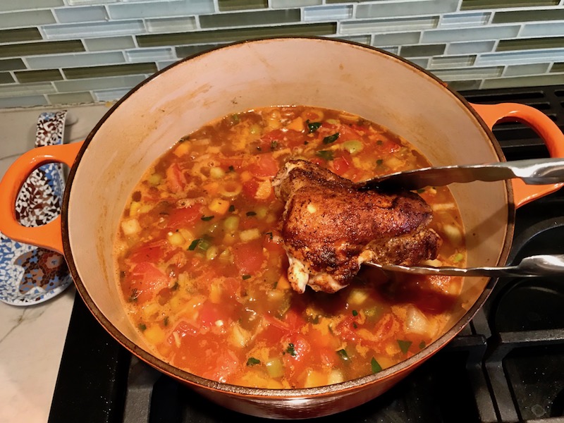 Adding chicken back to pot for Spanish Chicken and Rice. It's hearty, smokey, and delicious! Paprika spice blend rubbed chicken thighs are seared then cooked with rice, onions, carrots, garlic, tomatoes, and olives for unbelievable flavor! #easydinners #chickenrecipes