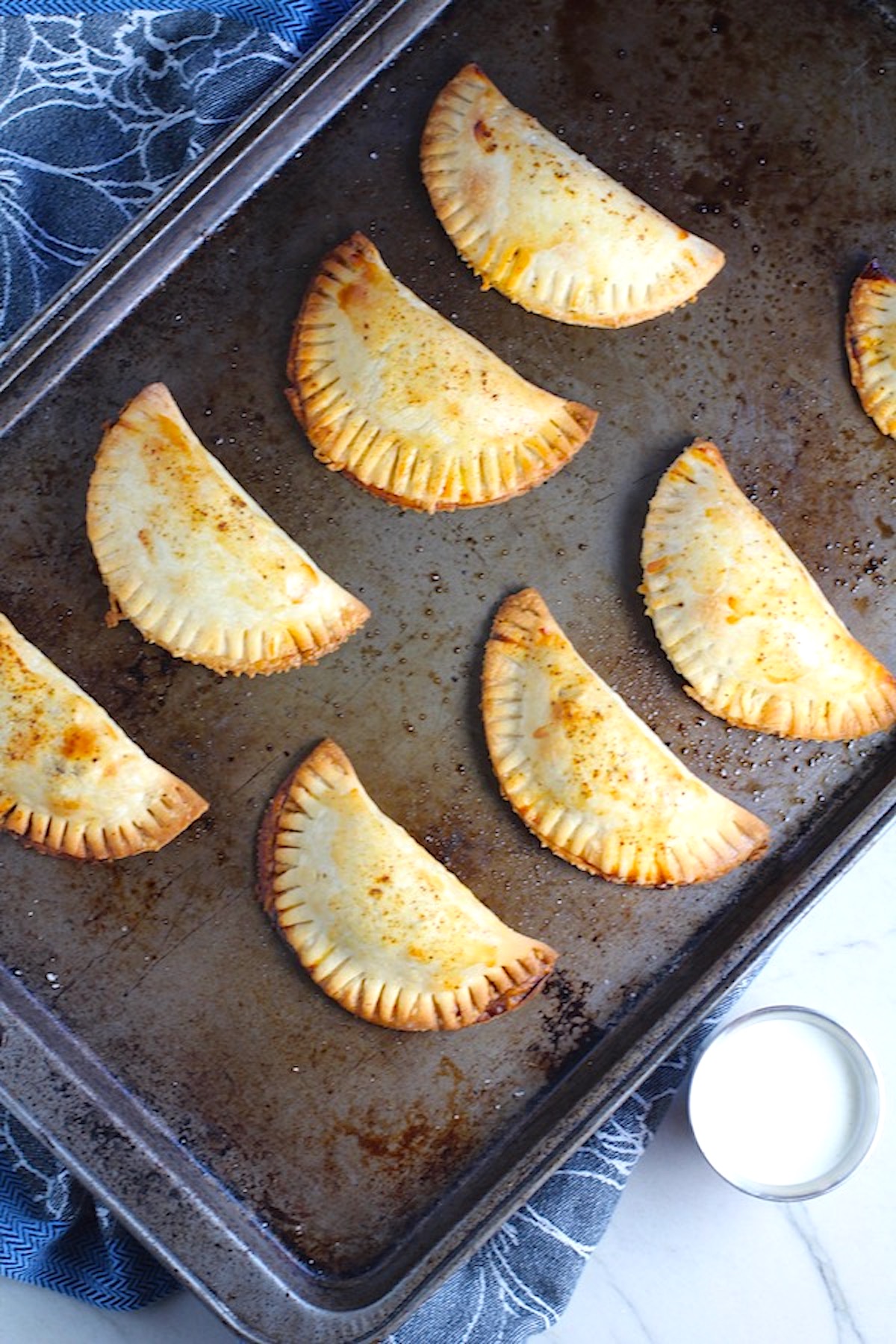 Ground Spiced Beef Empanadas cooked on a pan. Flaky, buttery pastry on the outside with a savory, smokey, salty ground beef filling.