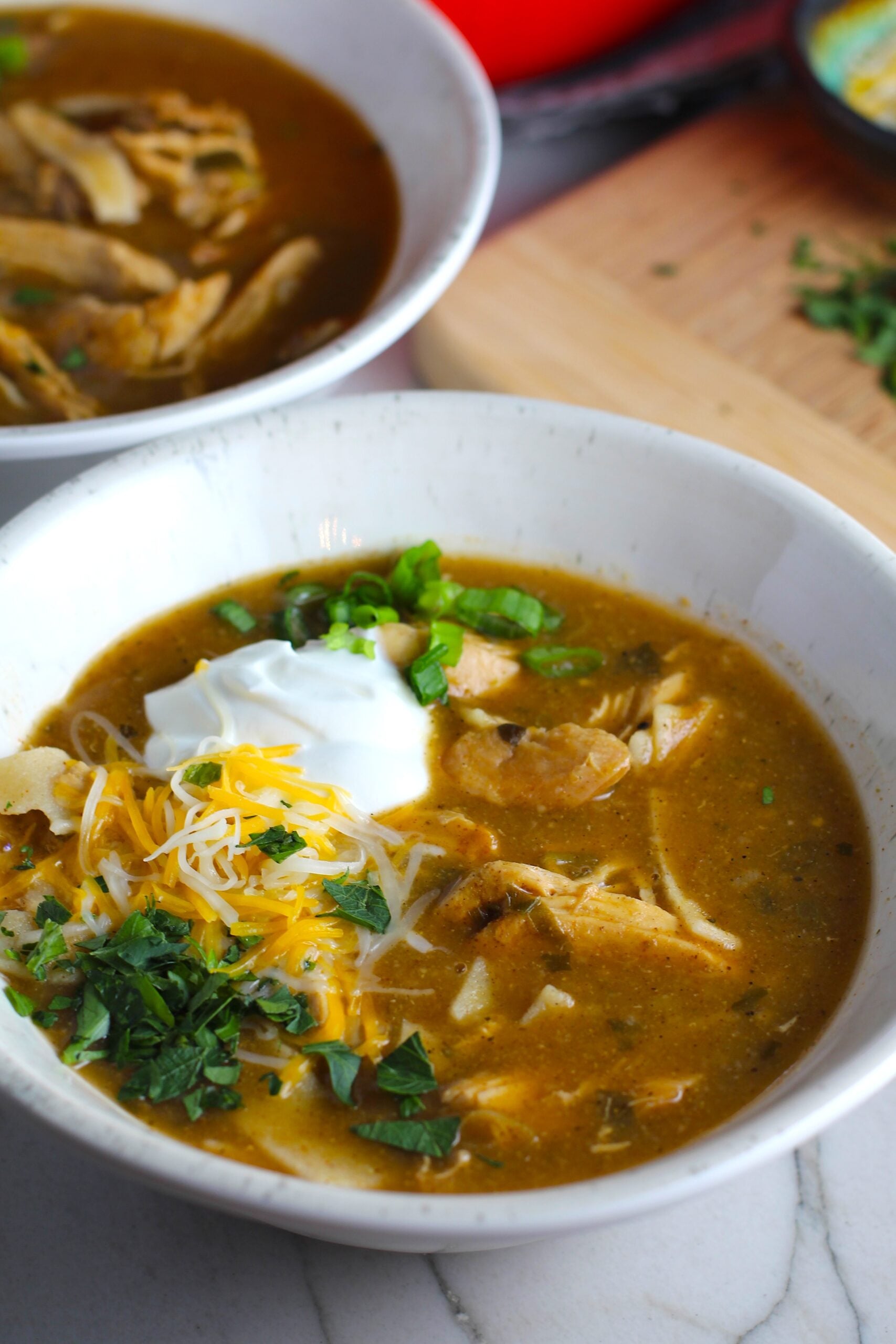 Creamy Chicken Enchilada Soup in a bowl topped with cheese, sour cream, and cilantro! It's creamy, hearty, slightly spicy with green chiles and smokey seasonings that bring so much depth. Corn tortilla strips act like the noodles in this soup!