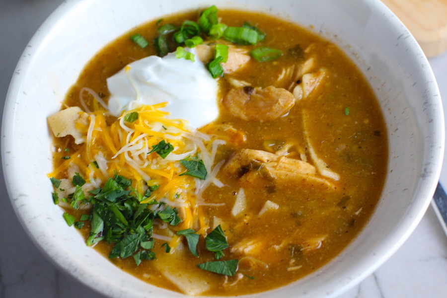 Creamy Chicken Enchilada Soup in a bowl topped with cheese, sour cream, and cilantro! It's creamy, hearty, slightly spicy with green chiles and smokey seasonings that bring so much depth.  Corn tortilla strips act like the noodles in this soup!