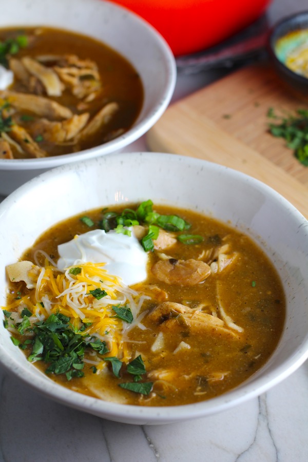 Creamy Chicken Enchilada Soup in a bowl topped with cheese, sour cream, and cilantro!  It's creamy, hearty, slightly spicy with green chiles and smokey seasonings that bring so much depth.  Corn tortilla strips act like the noodles in this soup!