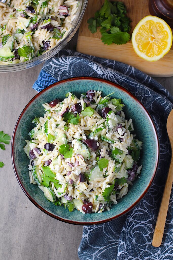 Greek Lemon Orzo Salad with Kalamata Olives, Cucumbers, and Feta Cheese in a bowl with lemon on side. It's mixed with a creamy lemon dressing that's bright and light!