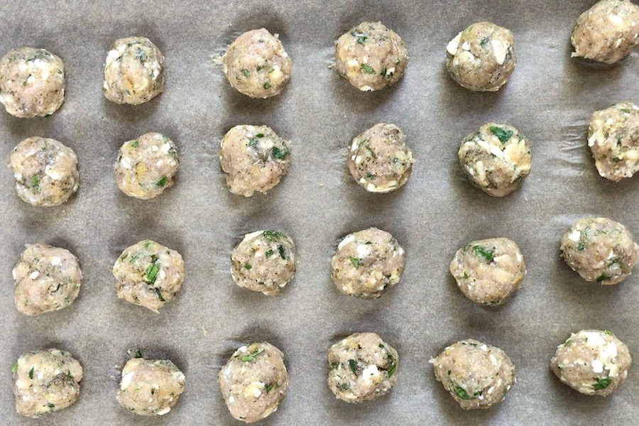 Raw Ground Chicken Greek Meatballs on a pan.  These meatballs have garlic, feta, parsley, and oregano