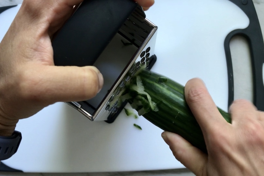 Grating cucumber for Tzatziki sauce to go with Chicken Greek Meatballs. These meatballs have garlic, feta, parsley, and oregano.