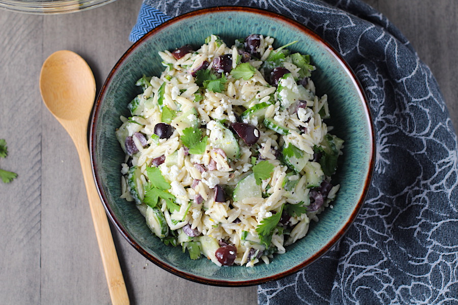 Greek Orzo Salad with Kalamata Olives, Cucumbers, and Feta Cheese in a bowl with spoon on side. It's mixed with a creamy lemon dressing that's bright and light!