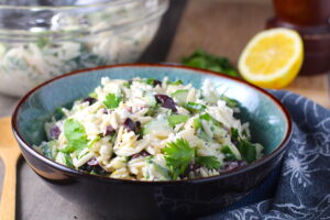 Greek Orzo Salad with Kalamata Olives, Cucumbers, and Feta Cheese in a bowl with lemon on side. It's mixed with a creamy lemon dressing that's bright and light!