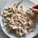 Hand shredding cooked chicken on a plate on counter for a BBQ Chicken Pizza Recipe