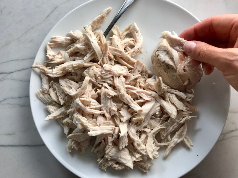 Hand shredding cooked chicken on a plate on counter for a BBQ Chicken Pizza Recipe