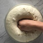 Hand punching down a homemade pizza dough in a bowl that had risen for a BBQ Chicken Pizza Recipe