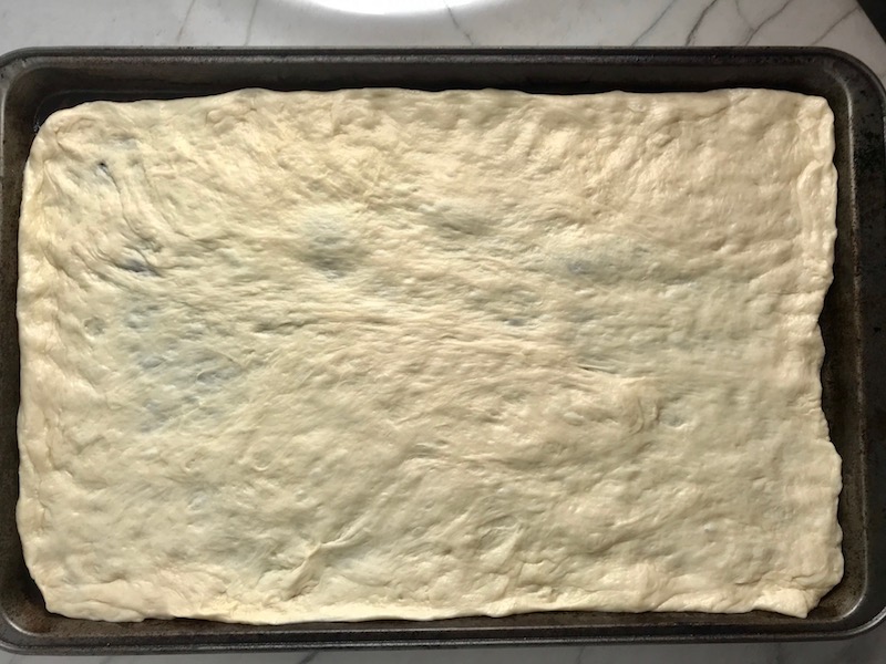Uncooked homemade pizza dough rolled and placed in a sheet pan for a BBQ Chicken Pizza Recipe