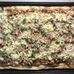 BBQ Chicken Pizza Recipe assembled on sheet pan with homemade pizza crust, creamy BBQ sauce, shredded bbq chicken, cheddar cheese, and cilantro.