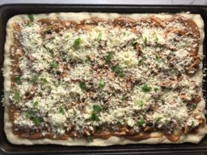 BBQ Chicken Pizza Recipe assembled on sheet pan with homemade pizza crust, creamy BBQ sauce, shredded bbq chicken, cheddar cheese, and cilantro.