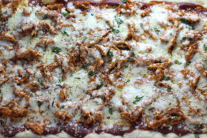 Whole BBQ Chicken Pizza in a rectangle sheet pan with homemade pizza crust, tangy and creamy BBQ sauce, hearty shredded chicken, cheddar cheese and coleslaw on top!   